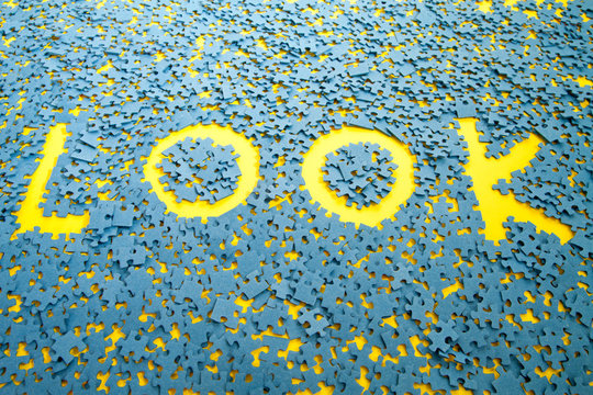 The word Look spelled out between blue jigsaw pieces on a table