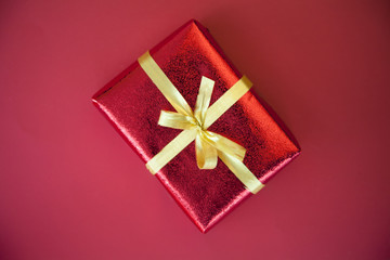 Overhead view of a red Gift box wrapped in ribbon with a gold bow on a red background