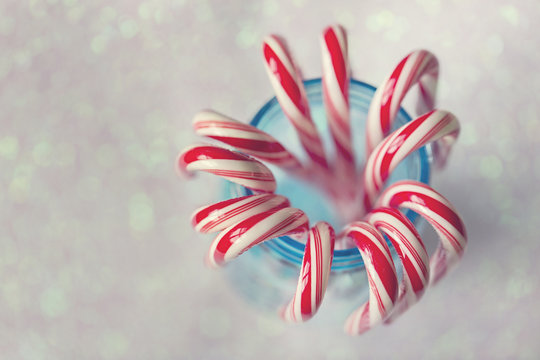 Red and white striped candy canes in blue mason jar against glittering background