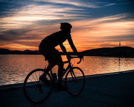 Close-up side view Silhouette of a cyclist cycling along the foreshore of Lake Burley Griffin at sunset, Canberra, Australia