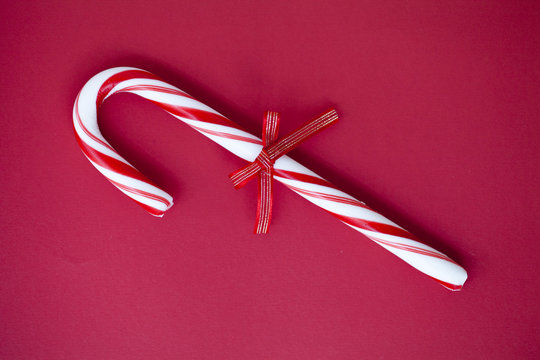 Overhead close-up of a candy Cane with a tied bow on a red background