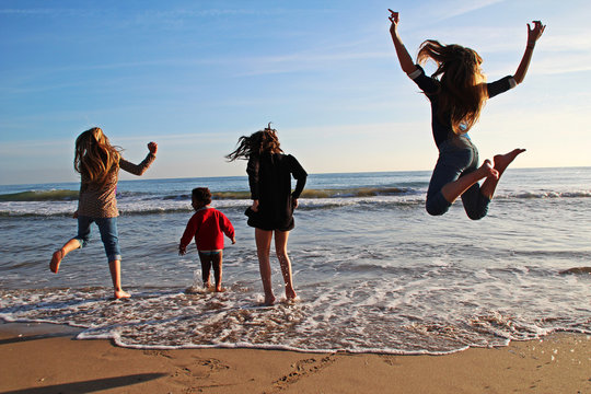Rear view of four girls jumping in the air and messing about on the beach, Castelldefels, Baix Llobregat, Barcelona, Catalonia, Spain