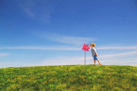 Boy standing in a field blowing on a tall pinwheel (whirligig) on a summer day
