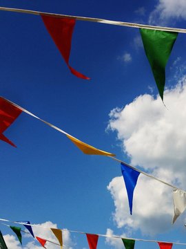 Close-up low angle view of Rows of multi coloured bunting against a partly cloudy blue sky