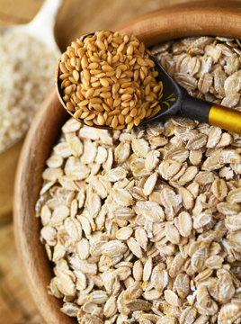 Close-up overhead view of a spoonful of golden flaxseeds and a bowl of organic rolled oats