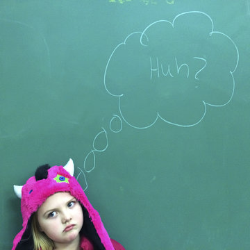 Girl (6-7) standing in front of blackboard with puzzled expression