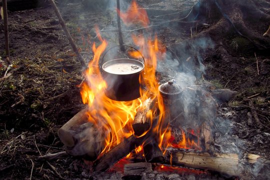 Close-up of a kettle and a cooking pot hanging over a campfire