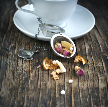 Tea strainer filled with marshmallow macaron herbal tea next to a tea cup on a wooden table