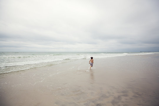 USA, North Carolina, Pender County, Topsail Beach, Boy (8-9) running away along beach on overcast day