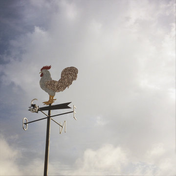 Weather vane against cloudy sky