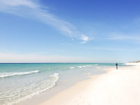 Distant view of a young man standing on beach fishing in Pacific Ocean, California, USA