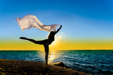 Fototapeta na wymiar Silhouette of girl with fiber dancing at sunset sea horizon