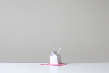 Conceptual milk carton with a straw on a table in a pool of pink strawberry milk