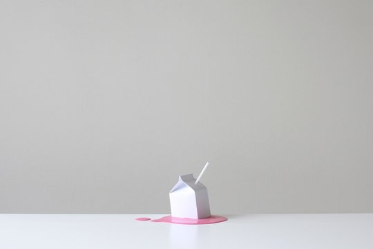 Paper carton with straw on spilled strawberry milk against white background