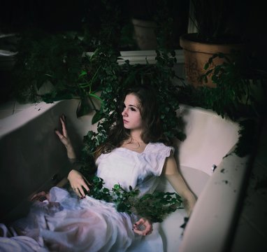 Young woman lying in a bath tub with lots of hands and vines