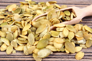Pumpkin seeds with spoon on wooden background