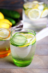 Fresh water with lemon and cucumber in glassware on wooden table, closeup