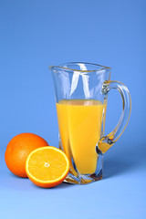 Glass pitcher of orange juice on blue background