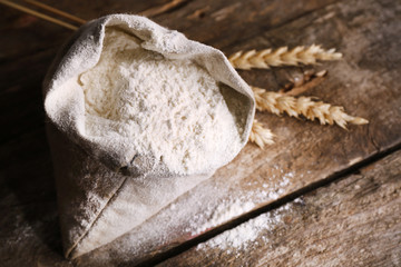 Bag of white flour with wheat ears on wooden background