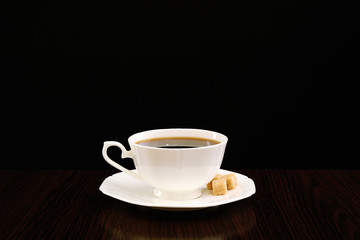 Cup of coffee with lump sugar on wooden table, on dark background