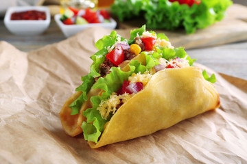 Tasty taco with vegetables on paper on table close up