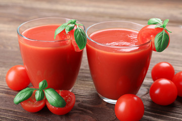 Glasses of tomato juice with vegetables on wooden background