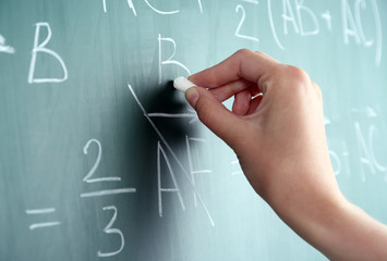 Female hand writing formulas on blackboard with chalk close up