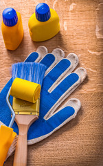 Paint roller brush bottles and protective gloves on wooden board