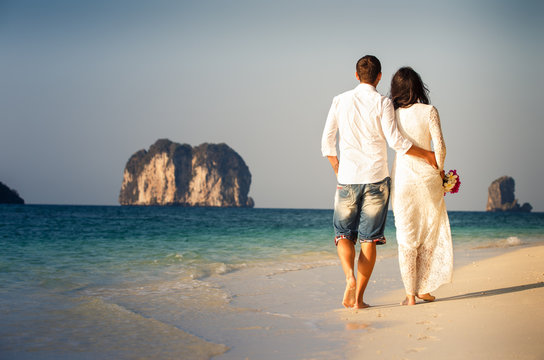 bride and groom walk barefoot on beach