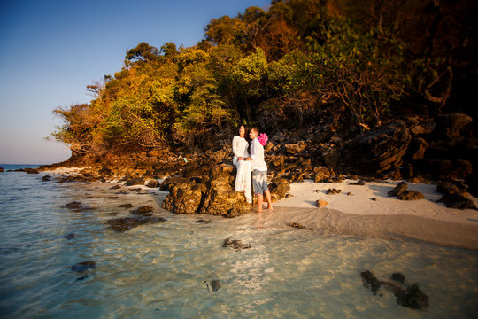 bride and groom at beach against rocks at sunrise