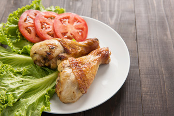 Grilled chicken legs and vegetables on wooden background.