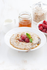 plate of oatmeal with fresh raspberries and honey on white 