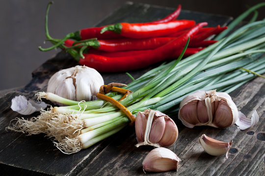 bunch of spring onions, red chili pepper and garlic on wood