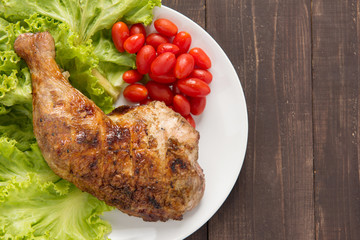 Grilled chicken legs and vegetables on wooden background.