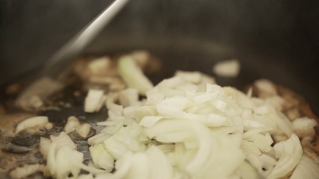 Chef pouring chopped onions into hot butter