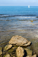 seashore with transparent sea and surfacing rocks with sailing b
