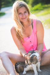 Young blonde woman playing with cat outdoor