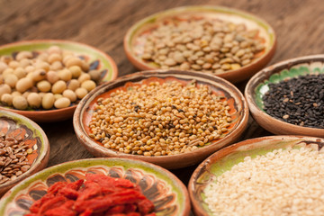 Various grain beans in small clay plates on natural textured woo