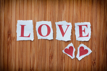 Word Love and two paper hearts on wooden texture background