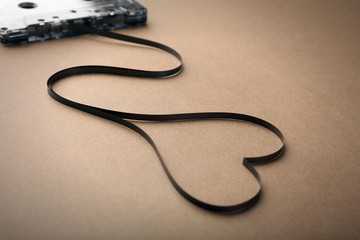 Audio cassette with magnetic tape in shape of heart on brown background