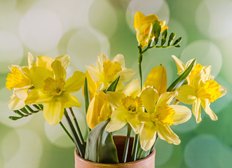 Yellow daffodils and freesias in a colored vase.