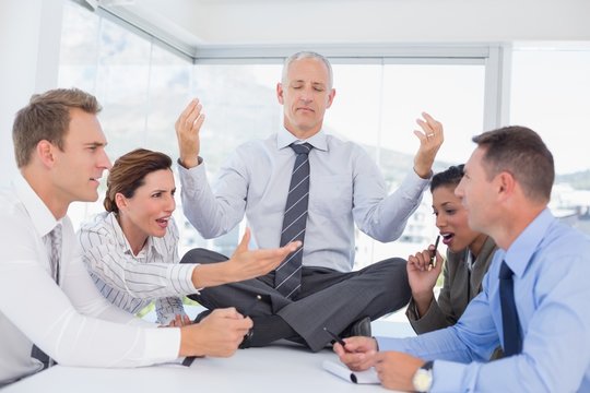 Businessman relaxing on the desk with upset colleagues around