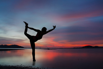 Silhouette of young woman practicing yoga on the lake at sunset