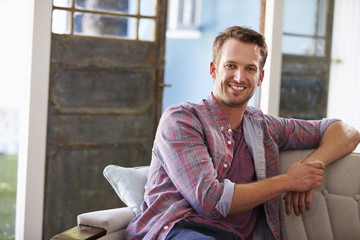 Portrait Of Smiling Young Man Sitting On Sofa At Home