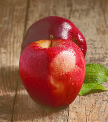 Two red apples with water drops on a wooden table, selective foc