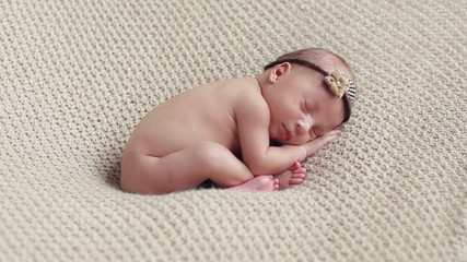 Adorable tiny newborn baby girl calmly and quietly sleeping lying curled up with her hands under head