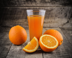 Orange juice glass and fresh oranges on wood