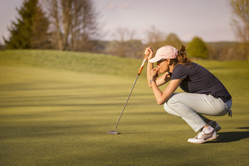 Female golf player squatting on green.