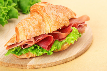 croissant filled with ham and lettuce on wooden chopping board