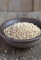 Dry green buckwheat in a clay bowl on wooden table